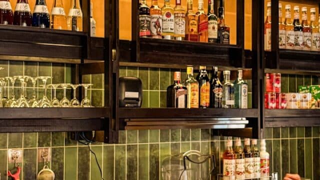 A bar counter at Uncle Huan Coffee with bottles, glassware, blenders, and a person's arm visible on the right side.
