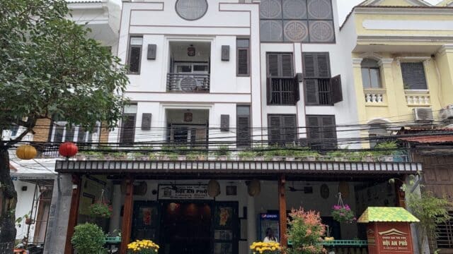Three-story white Vinh Hung Library Hotel with balconies, potted plants, lanterns, and parked motorbikes out front.