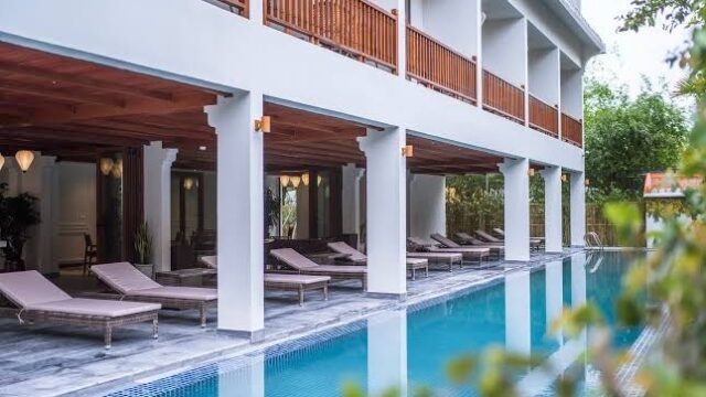 A modern hotel pool with lounge chairs and wooden balcony at Vinh Hung Old Town Hotel, surrounded by greenery in Hoi An.