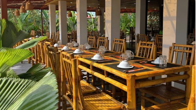 Outdoor restaurant Vườn Phố Hội features bamboo tables and chairs, set with plates and glasses, nestled amid lush greenery.
