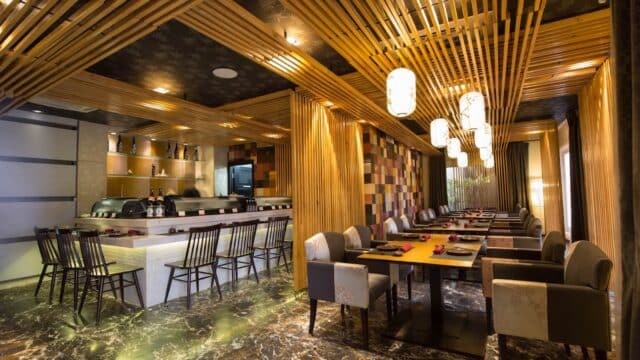Modern Wakaku Restaurant with wooden decor, marble floor, sushi bar, and tables set for dining under warm lighting.
