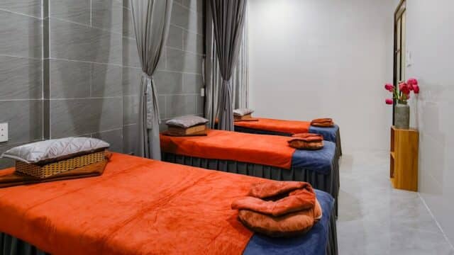 Three massage tables with orange covers and folded towels in a modern spa room, perfect for massages or relaxing while getting your nails done.