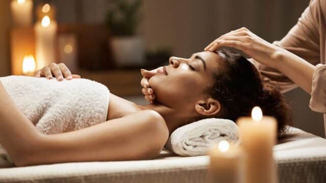 Woman lying on a massage table with candles around, receiving a relaxing head massage at You Beauty Spa.