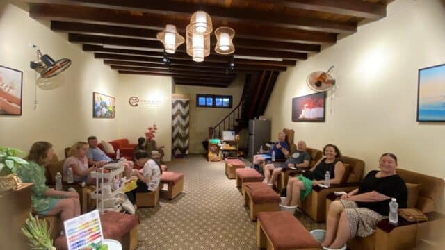 A group of people relax in a cozy Zen Nails spa, seated in chairs and receiving soothing foot treatments.