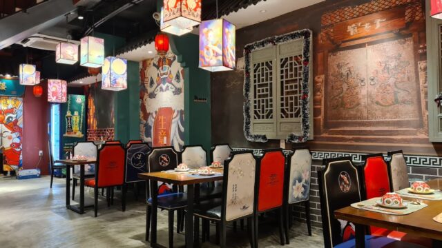 Colorful lanterns hang above tables and chairs in Zhong Hua Lou, a vibrant, ornately decorated Chinese restaurant interior.