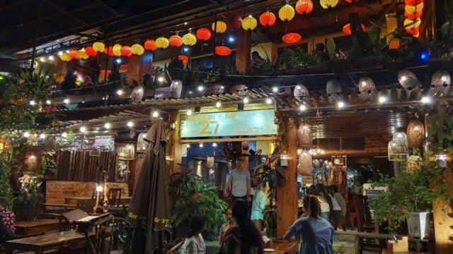 Outdoor bar at night in Hoi An, with colorful lanterns, people at wooden tables, and warm festive lighting.