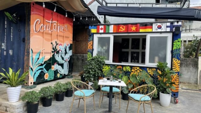Outdoor café in Hoi An with colorful murals, potted plants, and a small table with chairs on a concrete patio.
