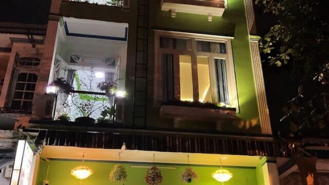 A brightly lit, green three-story building in Hoi An at night, with balconies and colorful lights on the rooftop.