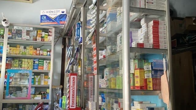A pharmacy in Hoi An with glass shelves filled with medicine boxes, bottles, and health products.