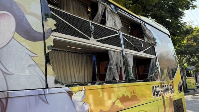 A yellow bus with broken windows, parked under trees in Hoi An, features animal artwork on its side.