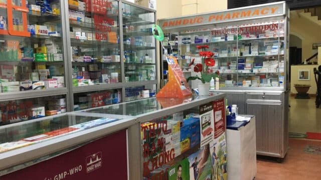 Interior of a Hoi An pharmacy with glass display cases filled with medicine boxes and products; signs in Vietnamese throughout.
