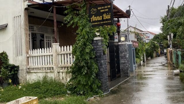 A rainy Hoi An street scene with a two-story house and a sign reading Anna Bùi near the entrance gate.