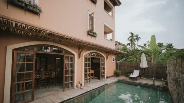 A peach-colored Hoi An house with large windows opens to a small backyard pool, lounge chair, and green plants.