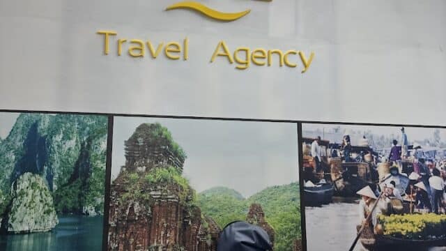 A wall with a yellow travel agency logo, Hoi An travel posters, and a golf bag placed in front.