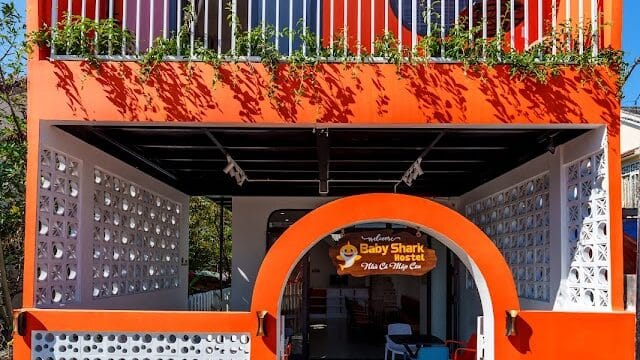Bright orange two-story Hoi An building with a balcony, white railing, arched entrance, and decorative block walls.