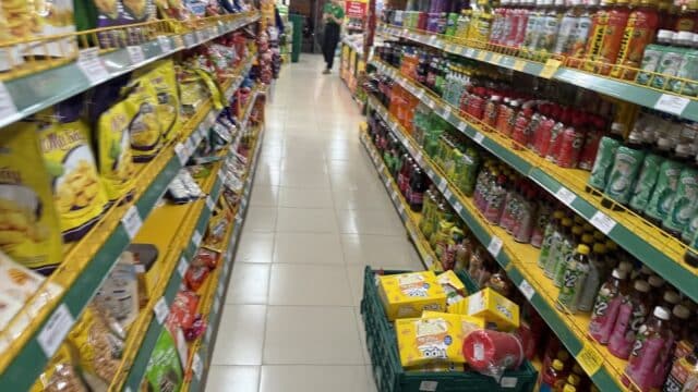 A grocery store aisle in Hoi An with snacks on the left, drinks on the right, and a crate of juice boxes on the floor.