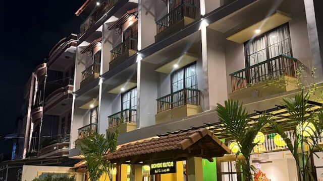 A three-story boutique hotel in Hoi An at night, warmly lit with balconies, lush plants, and an inviting entrance.