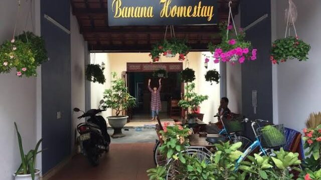 Entrance to Banana Homestay in Hoi An with hanging plants, potted greenery, and parked bikes and scooters.