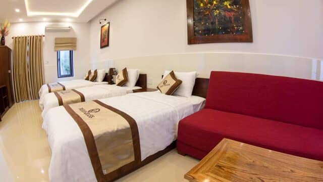 Hotel room in Hoi An with two single beds, a red sofa, wooden table, and a colorful painting on the wall.