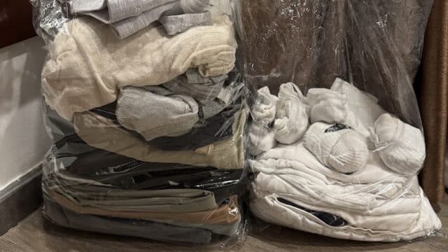 Two vacuum-sealed bags filled with folded clothes sit on a wooden floor next to a brown curtain in a cozy Hoi An home.