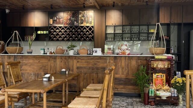 A cozy Hoi An café with wooden furniture, patterned tile floor, a wooden counter, decor, and a small altar with plants and flowers.