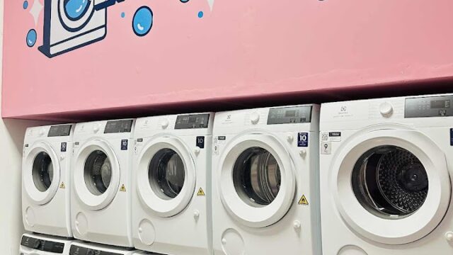 Ten white washing machines under a pink Laundromat sign with bubbles and a laundry icon in charming Hoi An.