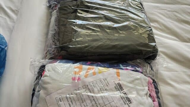 Three clear plastic bags of folded clothes from Hoi An on a bed, one with a paper receipt attached on top.