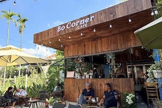 Outdoor café scene in Hoi An with people at tables, a wooden building, string lights, and a clear blue sky above.