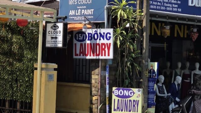 Street view in Hoi An: a yellow building with Laundry and Bóng Laundry signs, beside a paint store displaying mannequins inside.