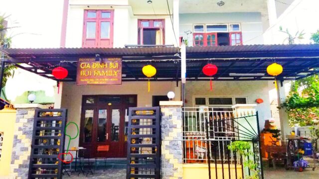 Two-story guesthouse in Hoi An with red lanterns, a yellow Bui Family sign, and a gated entrance on a sunny day.