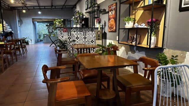 Cozy cafe interior with wooden table and chairs, potted plants, and a Hoi An-inspired patterned counter in warm lighting.