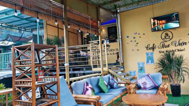 Outdoor seating area at Café Thư Viện in Hoi An with bamboo furniture, wall art, and a TV on a yellow wall.