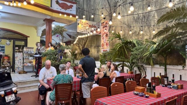 A group of people dine outdoors at a Hoi An restaurant under string lights, surrounded by lush plants.