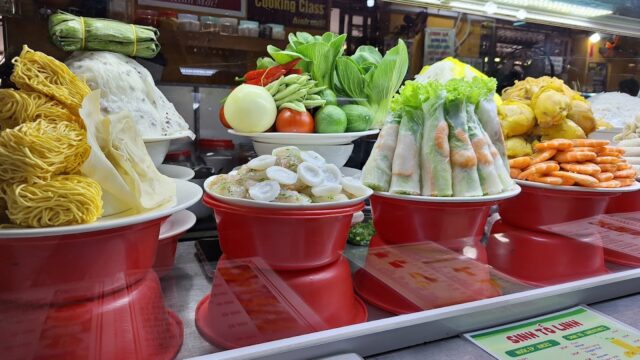 Plates of fresh Vietnamese ingredients and Hoi An specialties, including noodles, vegetables, spring rolls, and shrimp.
