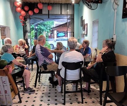 A group of people sit in a small, brightly lit room with teal walls and Hoi An-style red lanterns, engaged in conversation.