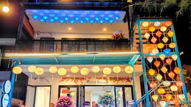 A brightly lit, three-story Chill Riverside Spa building in Hoi An, adorned with lanterns and neon signs glowing at night.