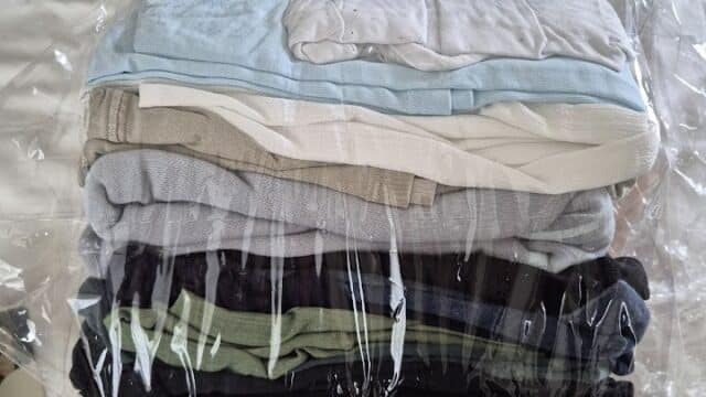 Neatly folded clothes, reminiscent of Hoi An’s tailor shops, stacked and wrapped in clear plastic on a white bedspread.
