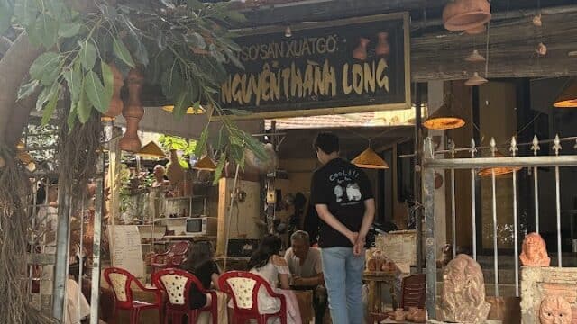 A man stands outside a rustic café in Hoi An, with people seated inside under a sign reading NGUYEN THANH LONG.