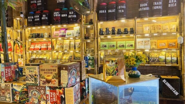 A cozy shop in Hoi An displays coffee and tea tins, colorful packets, and boxed products on wooden shelves.
