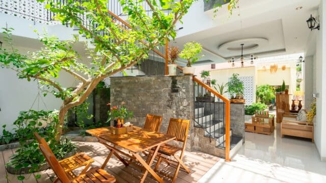 Sunny indoor garden in Hoi An with wooden table and chairs, lush green plants, and stairs leading to an upper floor.