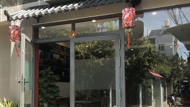 Glass entrance of a Hoi An hostel with red lanterns, lush plants by the door, and a weathered sign above the entrance.
