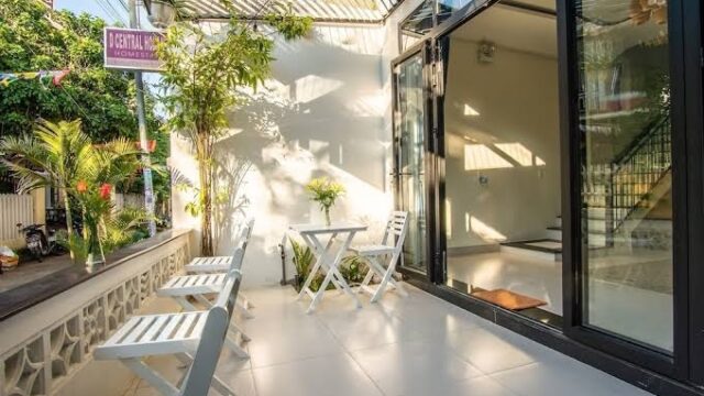 Sunny patio with white chairs, a small table, plants, and large glass doors evoke the relaxed charm of Hoi An living.