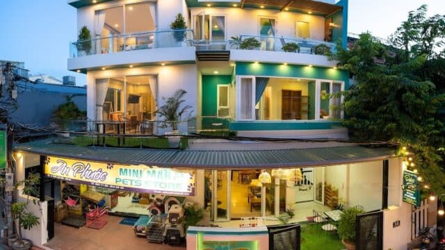 Two-story modern building in Hoi An with large windows, balconies, a mini mart, pet store, bikes outside, and greenery at the entrance.