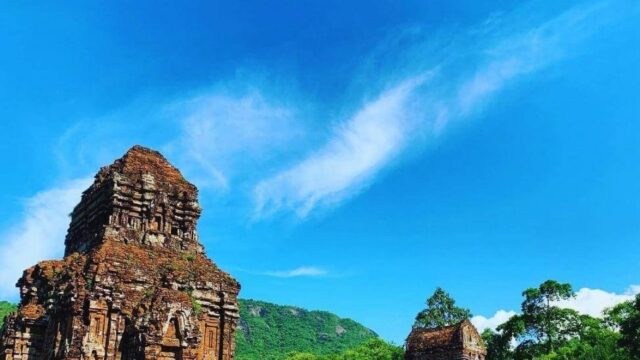 Ancient brick temple ruins near Hoi An, surrounded by lush green hills and a bright blue sky in the background.