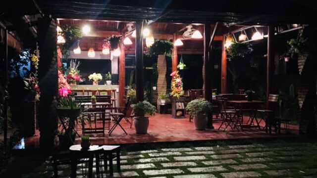 An outdoor patio at night in Hoi An, warmly lit, with wooden tables, chairs, and lush plants decorating the space.