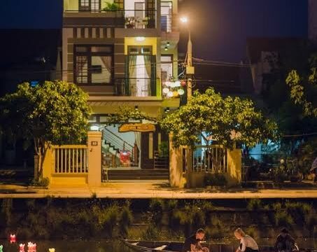 Three-story house by a canal at night in Hoi An, with people in boats and lanterns floating on the water.