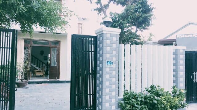 A gated Hoi An house with open doors, a tree in front, and a sign reading 576/A on a gray brick pillar.