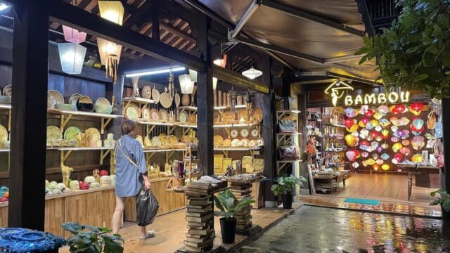A woman shops at a lantern-lit store in Hoi An, browsing crafts, baskets, and souvenirs on a rainy night.