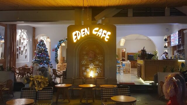 Eden Cafe in Hoi An at night, with outdoor seating, glowing sign, and a decorated Christmas tree visible inside.