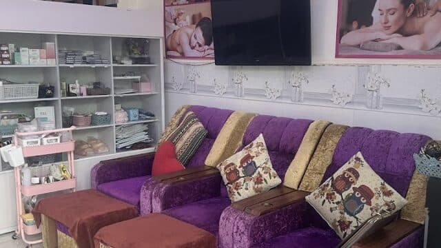 A cozy Hoi An spa lounge with purple and gold sofas, footrests, pillows, and massage posters on the walls.